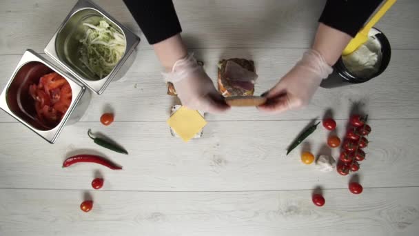 전문 요리사의 맨 위에는 패스트푸드 식당에서 맛있는 햄버거를 요리하는 모습이 그려져 있습니다. 장갑을 끼고 있는 여성 요리사가 빵 버거를 닫다 — 비디오