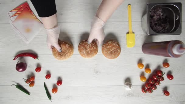Profesyonel şefin en iyi görüntüsü fast food restoranında lezzetli bir hamburger pişirir. Eldivenli kadın aşçı masada hamburger yemek için üç sakal açıyor. — Stok video