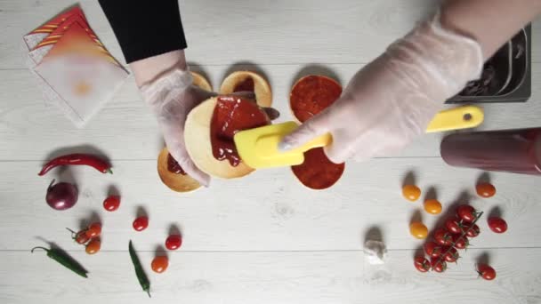 A vista superior do chef profissional cozinha um delicioso hambúrguer no restaurante fast food. chef feminino em luvas coloca ketchup em três pães enferrujados para hambúrgueres — Vídeo de Stock