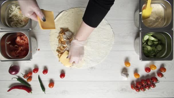 Chef-Hände in weißen Handschuhen legen Käse auf Dönershawarma in Pita oder Lavasch. Shawarma mit Hühnchen, Pommes, Käse und Gemüse kochen — Stockvideo