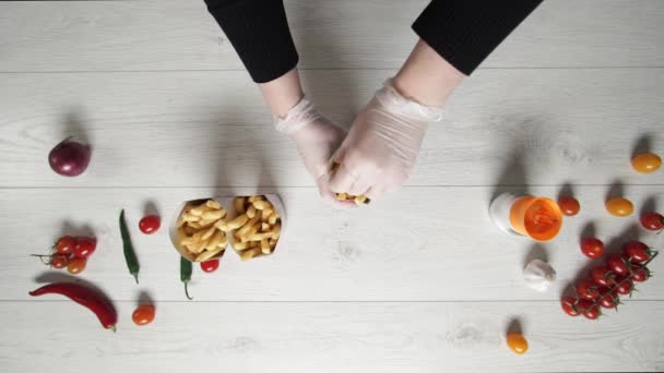 Шеф-повар в перчатках перемещает горячую и вкусную картошку фри в бумажный пакет — стоковое видео