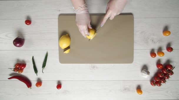 Chef manos en guantes cortando un limón en la tabla de cortar. Limón rebanado a mano en primer plano de la tabla de cortar. Limón jugoso cortado en rodajas. El cuchillo de chef afilado corta los cítricos . — Vídeos de Stock