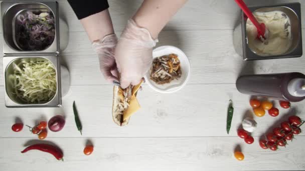 Top view of hands of professional chef in gloves making shawarma on sandwich in bread. Chef in gloves puts french fries and chicken meat in sandwich — Stock Video