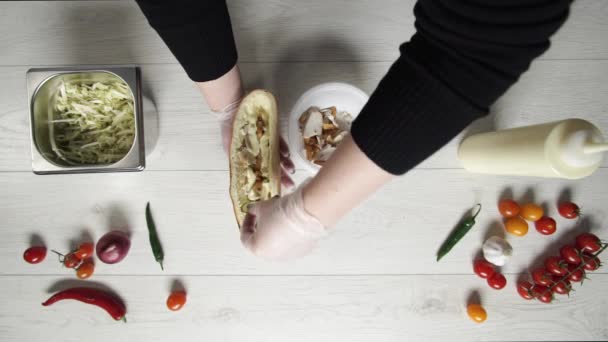 Góra widok rąk profesjonalnego szefa kuchni w rękawiczkach podejmowania shawarma na kanapkę w chlebie. Szef kuchni w rękawiczkach wkłada ogórki do kanapki — Wideo stockowe
