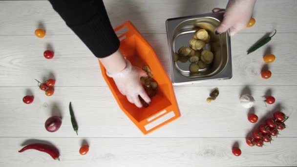 Le chef prend une tranche de cornichons dans un bol en plastique et les met dans un récipient en métal. 
