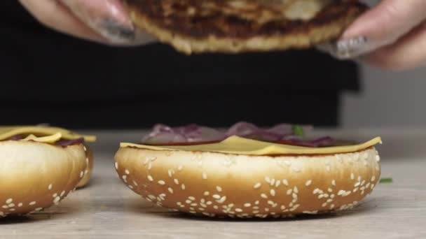 Der Chefkoch kocht im Fast-Food-Restaurant drei verschiedene leckere Burger. Köchin in Handschuhen legt gegrilltes Schweinefleisch auf Burger — Stockvideo