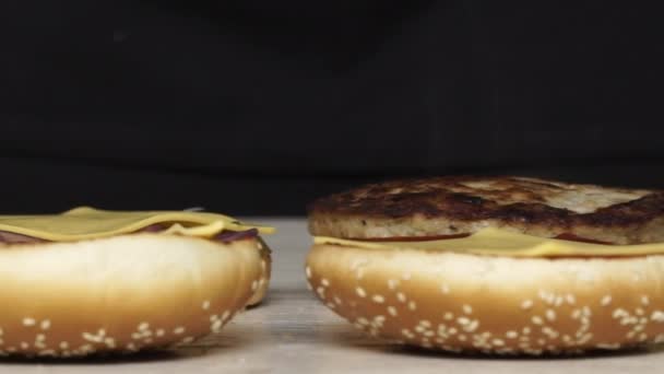 A vista superior do chef profissional cozinha três diferentes hambúrgueres deliciosos no restaurante fast food. Chef feminino em luvas coloca carne grelhada no hambúrguer — Vídeo de Stock