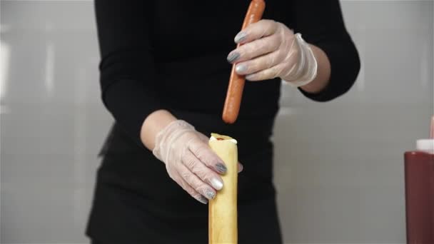Chef manos en guantes cocina un hot dog francés, salchicha en la masa. Chef pone salchicha en el interior de la salchicha francesa — Vídeo de stock