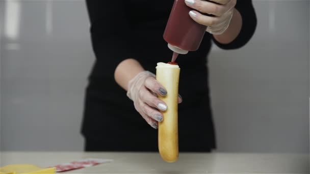 Chef hand in hand handschoenen kookt een Franse hotdog, worst in het deeg. Chef schenkt ketchup bovenop de hotdog — Stockvideo