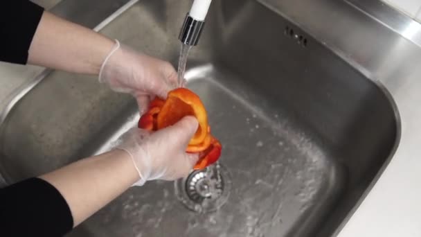 Wash the fruit. Woman above the sink under the water washes red bell pepper — Stock Video