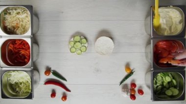 Profesyonel şef fast food restoranında lezzetli bir hamburger pişiriyor. Eldivenli kadın aşçı hamburgerin üstüne domates koyar.