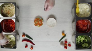 Profesyonel şef fast food restoranında lezzetli bir hamburger pişiriyor. Eldivenli kadın aşçı hamburgerin üstüne lahana koyar.