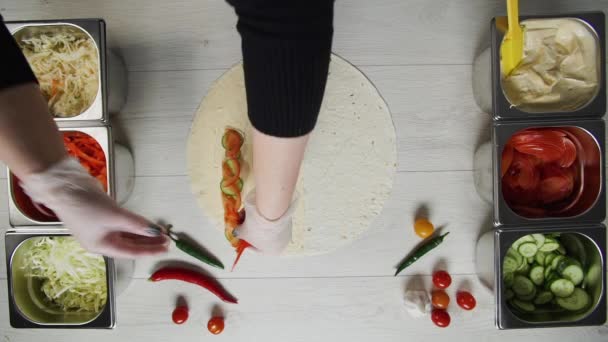 Von oben betrachtet legt der Koch in weißen Handschuhen Paprika auf Dönershawarma in Pita oder Lavasch. Shawarma mit Hühnerschnitzel, Paprika, Käse und Gemüse — Stockvideo