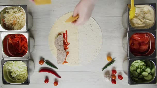 Vista dall'alto di mani di chef in guanti bianchi mette il formaggio su doner kebab shawarma in pita o lavash. Shawarma con costoletta di manzo, papaveri, formaggio e verdure — Video Stock