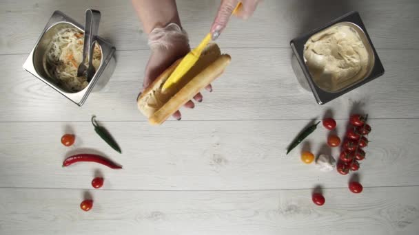 Profesyonel şef fast food restoranında lezzetli bir sandviç pişiriyor. Eldivenli kadın aşçı sandviçe sos koyar. — Stok video