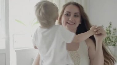 Mutlu, genç anneye yakın. Neşeli, güler yüzlü bebeğini yanıltıcı oturma odasında döndürür..