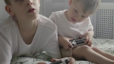 Beyaz tişörtlü iki küçük kardeş, yatakta oturup oyun kağıtlarıyla TV 'de oyun oynuyorlar.