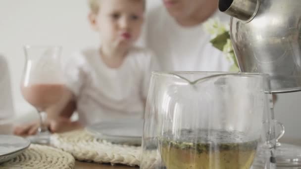 Primer plano de la familia desayunando. Madre vertiendo un agua caliente a la tetera — Vídeos de Stock