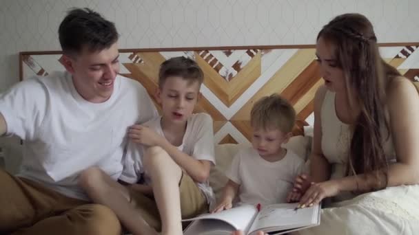 家族のお母さん、お父さんと2人の兄弟がソファに座って本を読んで閉じます。家族読書時間. — ストック動画