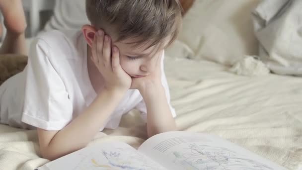 Genç bir çocuk yatağa uzanıyor ve kitap okuyor. — Stok video