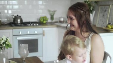 Mutlu anne ve küçük oğlu annelerinin dizlerinin üstüne çöküp sabah kahvaltısını yapıyorlar.
