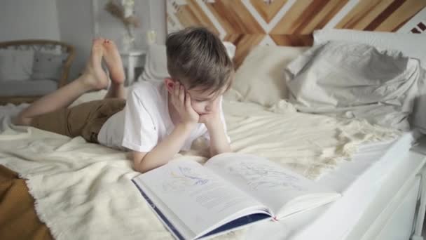 Підлітковий хлопчик лежить на ліжку і читає книгу — стокове відео