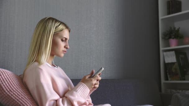 Közelkép szomorú fiatal nő olvas egy rossz hír, és dobja a telefont, miközben ül a kanapén otthon — Stock videók