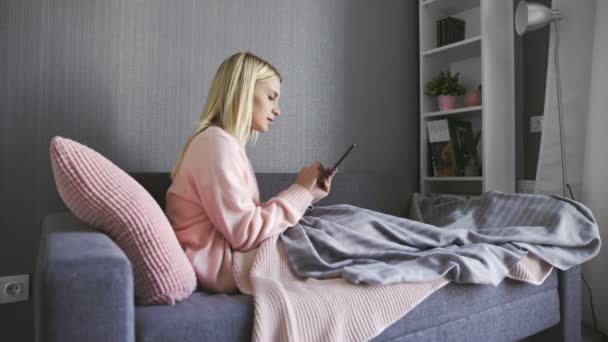 Gelukkig vrouw spelen het spel op tablet zitten op een bank thuis — Stockvideo
