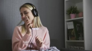 Kulaklık takan, mutlu müzik dinleyen ve kanepede dans eden bir kadın.