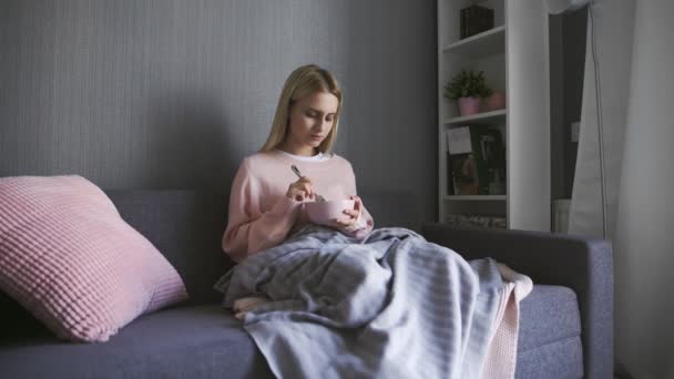 Mujer joven se sienta en el sofá y sostiene el tazón con ensalada — Vídeos de Stock