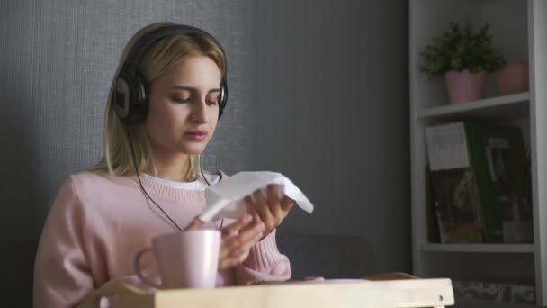 Zblízka mladá žena sedí na gauči jí toast s čokoládovou pomazánkou a poslouchat hudbu na smartphone — Stock video