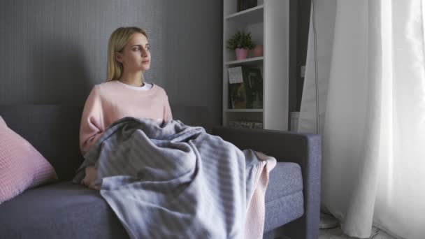 Mujer joven se sienta en el sofá gris y bebe un té — Vídeos de Stock