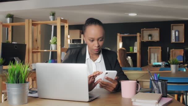 Νεαρή αφροαμερικανή γυναίκα που χρησιμοποιεί το τηλέφωνο κοιτάζοντας την οθόνη surfing social media στο γραφείο — Αρχείο Βίντεο