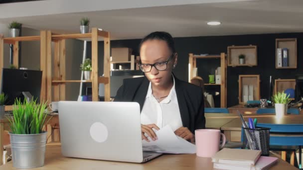 Elégedetlen afro-amerikai nő szemüvegben dolgozik notebook és dokumentumok — Stock videók