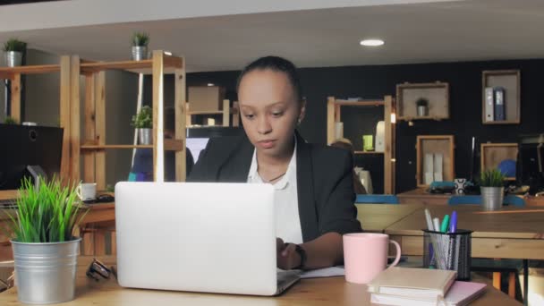 Νεαρή Αφροαμερικανή δακτυλογραφεί σε φορητό υπολογιστή και πίνει καφέ από ένα ροζ κύπελλο — Αρχείο Βίντεο