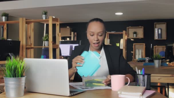 Een jonge Afro-Amerikaanse vrouw die luncht op kantoor. Vrouw eet groenten uit container — Stockvideo