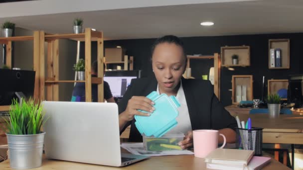 Jovem afro-americana almoçando no escritório. Mulher não quer come legumes de seu recipiente — Vídeo de Stock