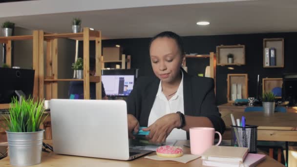 Una joven afroamericana almorzando en la oficina. La mujer no quiere comer verduras, ella decidió comer donut — Vídeo de stock