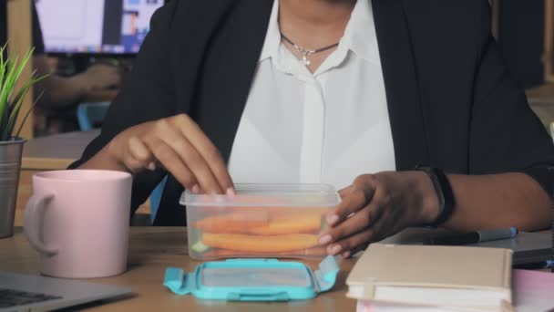 Primer plano de una joven afroamericana almorzando en la oficina. Mujer come verduras de su contenedor — Vídeos de Stock