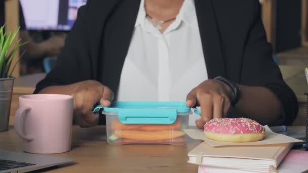 Primer plano de una joven afroamericana almorzando en la oficina. Mujer come verduras de su contenedor — Vídeos de Stock