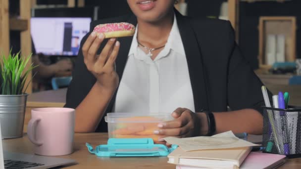 Κοντινό πλάνο μιας νεαρής Αφροαμερικανής που γευματίζει στο γραφείο. Η γυναίκα δεν θέλει να φάει ντόνατ, αποφάσισε να φάει λαχανικά. — Αρχείο Βίντεο