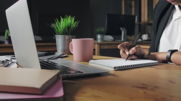 Nahaufnahme einer Afroamerikanerin, die im Büro in Notizbuch schreibt — Stockvideo