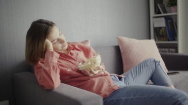 Genç bir kadın kanepede oturuyor, patlamış mısır yiyor, televizyon izliyor ve sızıyor.