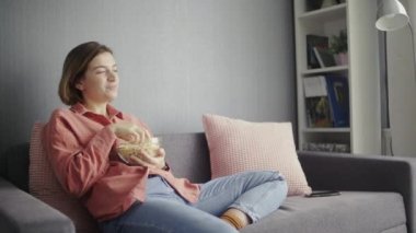 Genç, mutlu bir kadın kanepede oturuyor ve televizyonda komedi filmi izliyor.