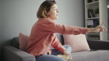 Genç, heyecanlı bir kadın kanepede oturuyor, arkadaşıyla konuşuyor ve TV seyrediyor.