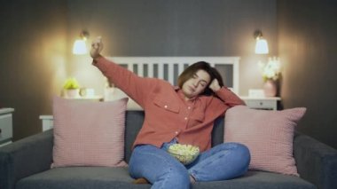Uykulu kadın kanepede oturuyor, patlamış mısır yiyor ve televizyon seyrediyor.