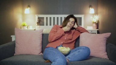 Kanepede oturup patlamış mısır yiyen ve televizyon izleyen sıkıcı bir kadın.