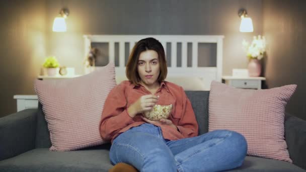 Ung kvinna sitter i soffan, äter popcorn, tittar på TV och faller alseep — Stockvideo