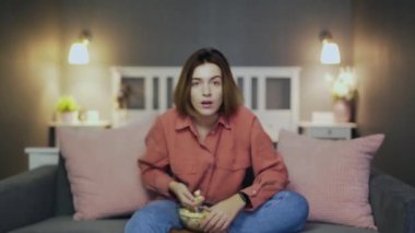 Kanepede oturup patlamış mısır yiyen, futbol maçı izleyen heyecanlı bir kadın.