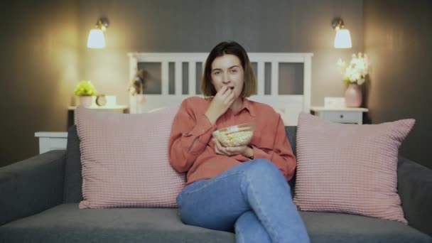 Gelukkige jonge vrouw zittend op de bank, popcorn etend, komedie film kijkend en lachend — Stockvideo